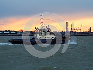 Harbor tug makes its way up the river back to port against an orange sunset