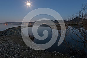 An harbour on a lake at dusk with star shaped moon