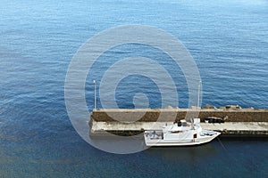 Harbour and small white fishing boat tied to the pier in the Mediterranean Sea with blue sea waters on the background.