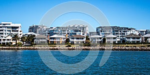 Harbourside condominium apartments behind free standing houses with grass frontage, stone retaining wall and blue river against bl photo