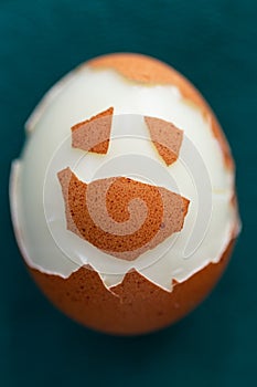 Hard-boiled half unshelled chicken egg on green background. Funny face made of eggshell on the surface.