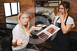 Hard choise Confused blonde young woman can`t choosing color hair from palette before coloring in beauty salon. Beauty