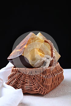 Hard craft cheese in a brown wicker basket. Chunks of hard cheese on a black background. Vertical photo