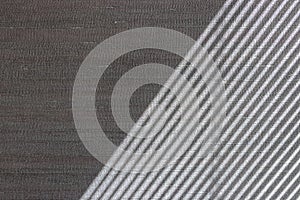 Hard diagonal shadows on grey textured wall from a window roller shutter or blinds. Attractive abstract half frame composition