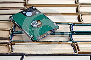 Hard drive on a stack of old shabby paper books. Comparison of storage media volumes of different eras