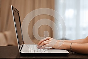 The hard hands of a businessman are typing on a laptop keyboard against the background of a blurred room. Concept for workplace,