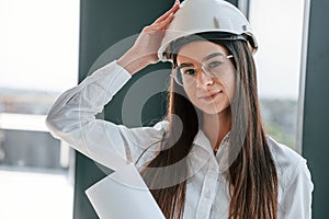 In hard hat, with plan in hands. Young woman is on the construction site