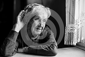 A hard of hearing old woman puts her hand to her ear. Black-and-white photo.