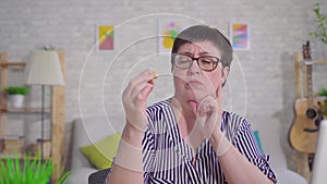 Hard of hearing thoughtful woman holding a hearing aid sitting in the living room