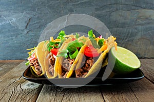Hard shelled tacos with ground beef, vegetables and cheese on a dark background photo