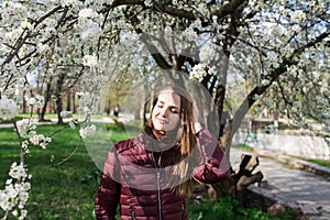 A hard sunbeam falls on the girl`s face. The girl is dressed in a jacket marsala color and a brown scarf.