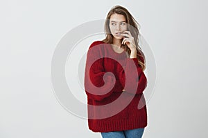 It is hard to refrain from sweets. Good-looking girl office worker in loose red sweater holding fingers in lips while