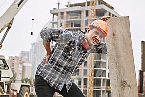 Hard work. Construction worker in protective helmet feeling back pain while working at construction site. Building