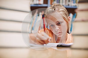 Hard at work. A cute young girl doing schoolwork while surrounded by books at the library.