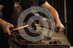 Close-up working powerful hands of male blacksmith forge an iron product in a blacksmith. Hammer, red hot metal and