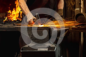 Close-up working powerful hands of male blacksmith forge an iron product in a blacksmith. Hammer, red hot metal and