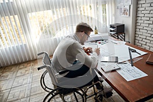 Hard work. Side view of busy male engineer in a wheelchair sketching a construction project while working at his