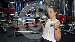 A hard-working girl is training her arms with dumbbells