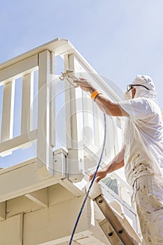 Hard Working House Painter Spray Painting A Deck of A Home