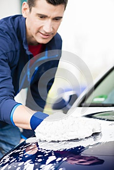 Hard-working man polishing car with white microfiber mitt