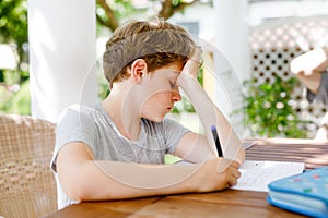 Hard-working sad school kid boy making homework during quarantine time from corona pandemic disease. Upset tired child