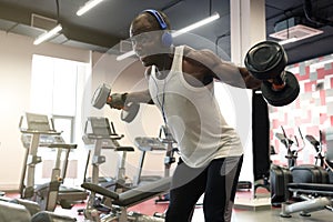 Hard workout. Muscular black man doing exercises with dumbbells at gym