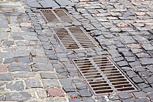 Hardscape sett road with iron grate of the drainage system hatch. photo