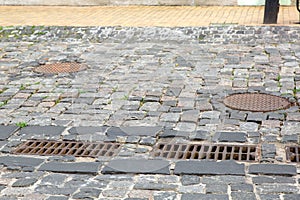 Hardscape sett road with iron grate of the drainage system hatch. photo