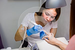 Hardware manicure in a salon. Manicurist is applying electric nail file drill