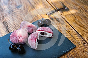 A hardwood table with a slate cutting board displaying pink mochi and cherries