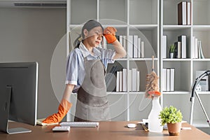 A hardworking Asian woman puts rubber gloves and cleaning equipment on her forehead. shows fatigue from Clean the office