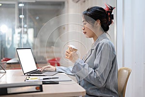 A hardworking businesswoman sipping coffee while working on her project on her laptop in her office