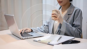 A hardworking businesswoman sipping coffee while working on her project on her laptop in her office