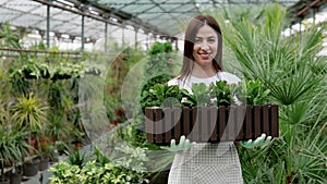 Hardworking farmer woman in a greenhouse holding box with flower pots. Home gardening, love of plants and care. Small business.