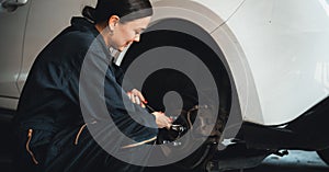 Hardworking female mechanic changing car wheel in auto repair workshop. Oxus