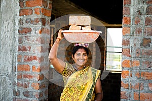 hardworking Indian smiling women with bricks on head looking at camera - concept of daily wagers lifestyle, positive photo