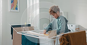 A hardworking little smiling boy helps his mom in the laundry room with household chores. The child pulls clothes from