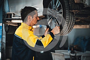 Hardworking mechanic changing car wheel in auto repair workshop. Oxus