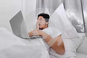 Hardworking people concept. Tired overworked young Asian man sleeping with computer laptop on the bed in bedroom