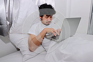 Hardworking people concept. Tired overworked young Asian man sleeping with computer laptop on the bed in bedroom