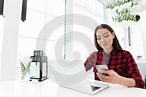 Hardworking woman using smartphone while working with laptop