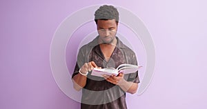 hardworking young african man reading novel isolated on violet background.