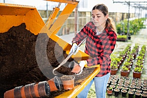 Hardworking young farmer woman fills a flower pot with nutritious soil