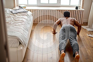 Hardwworking man performs pushup on floor in the bedroom