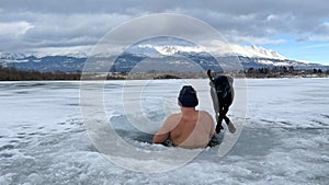 hardy man in ice water with snow with black dog