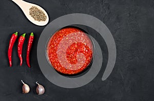 Harissa sauce on a black background. Adjika hot chili peppers sauce. Copy space, top view, flat lay