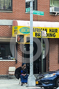 Harlem, New York, USA - June 10, 2017: African american woman waiting for clients in african hair braiding hairdressing in Harlem