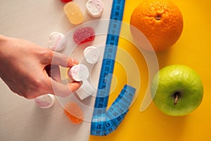 harmful marmalade candies and healthy fruits on opposite sides of the measuring tape