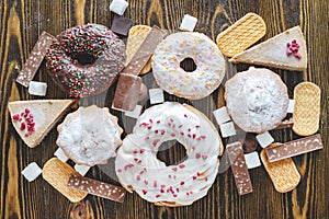 Harmful sweet foods on a dark wooden background. Donuts and muffins on the table pile. Unhealthy diet and overweight