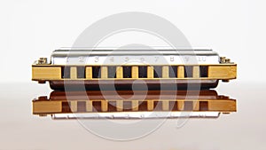 The harmonica lies on a mirrored surface. Classical musical wind instrument